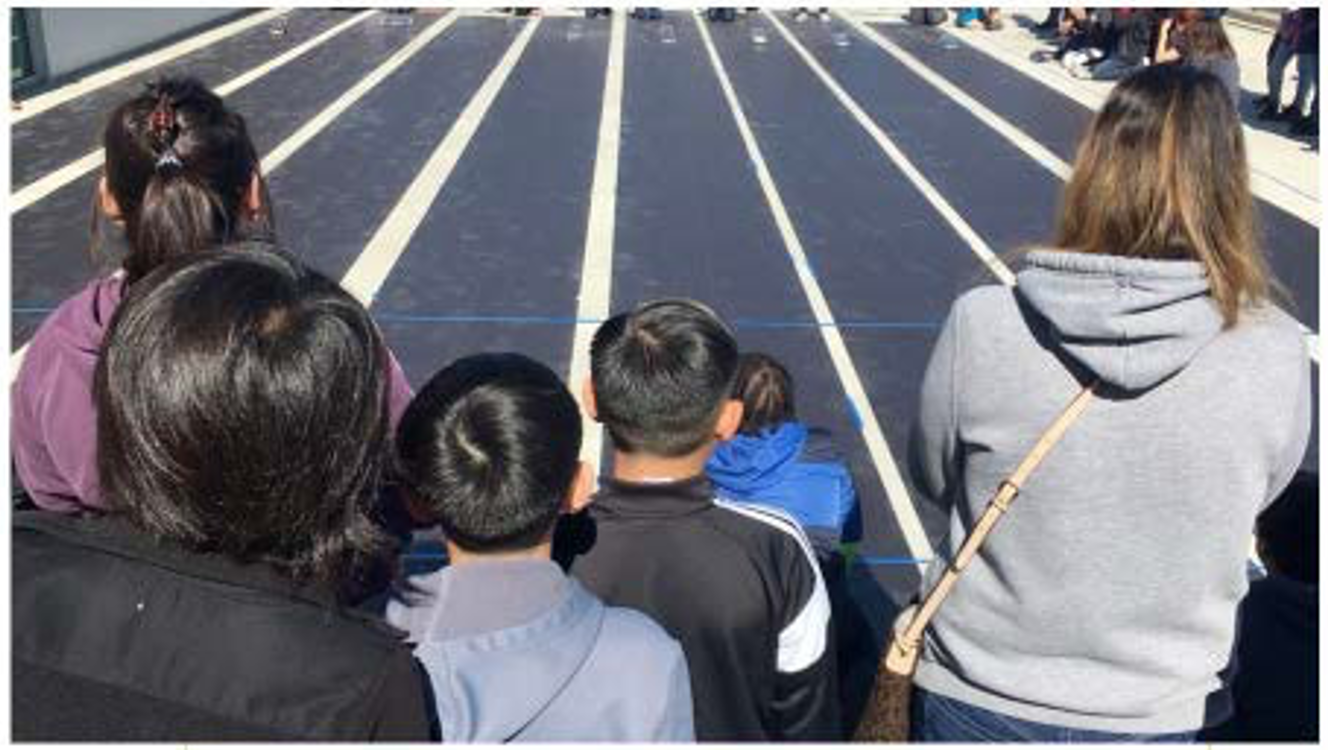 Students watch as solar cars start down the track during the Solar Car Challenge race event for middle school teams